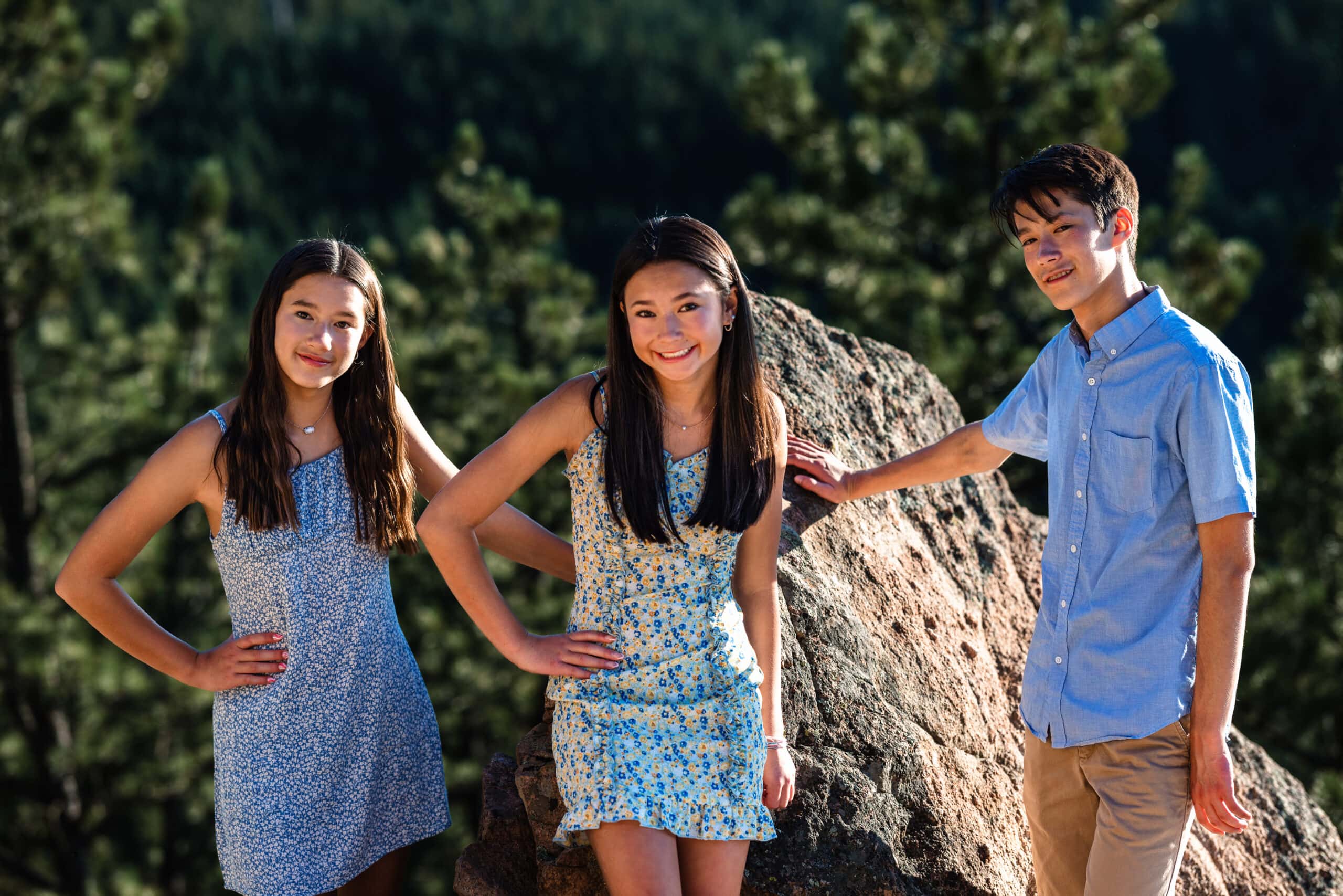 Three teens smiling by a sunlit boulder in a Colorado family portrait