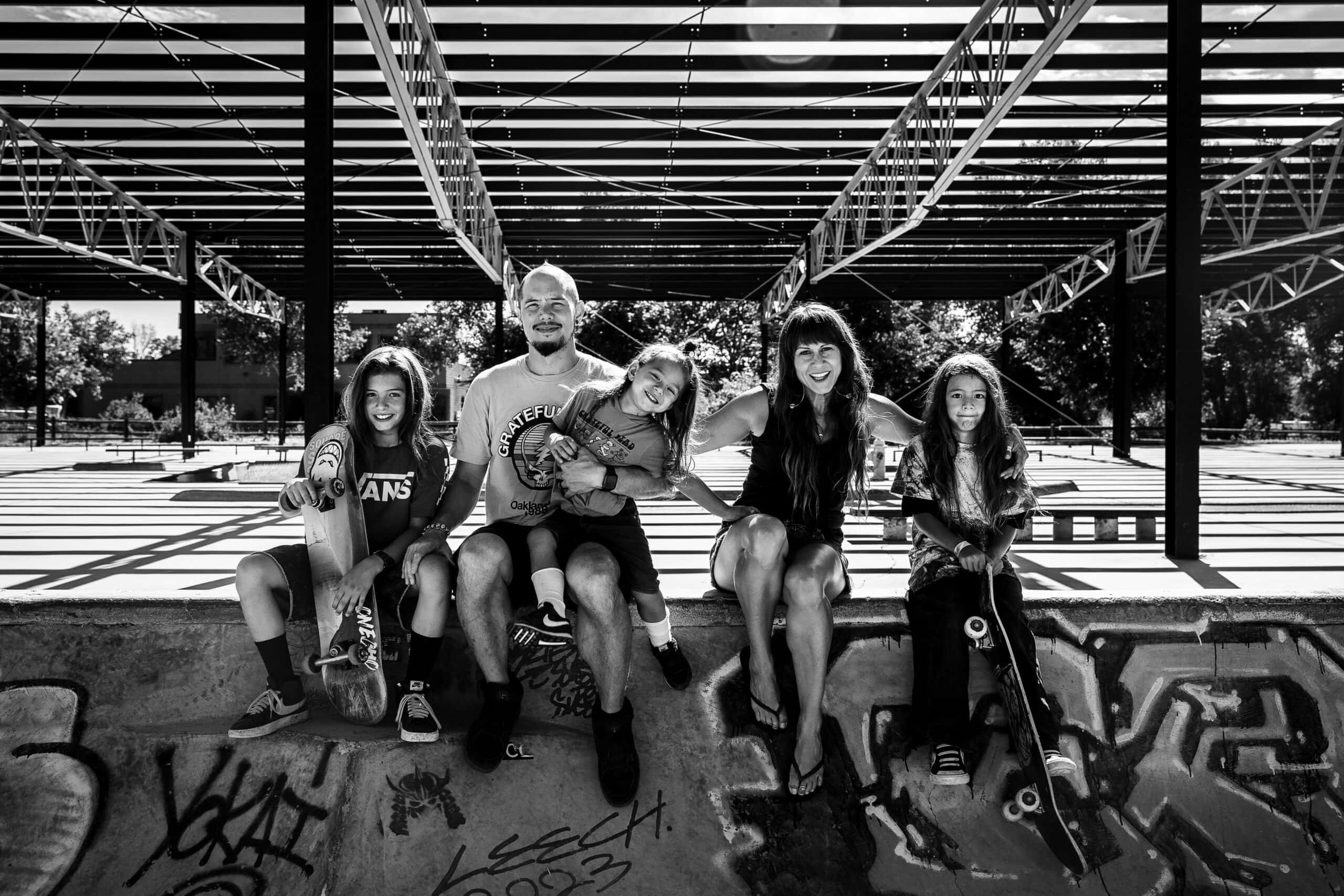 Black-and-white Colorado family portrait at graffiti-covered skatepark under pergola shadows