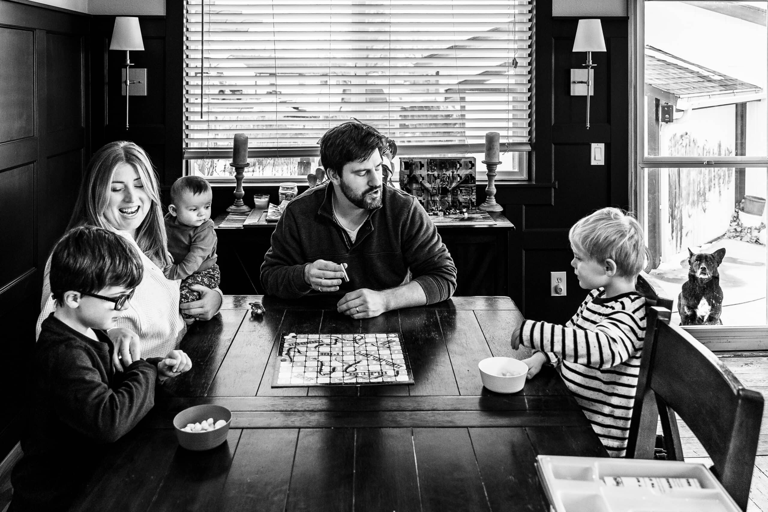 Black-and-white family playing a board game at home with baby and cat.