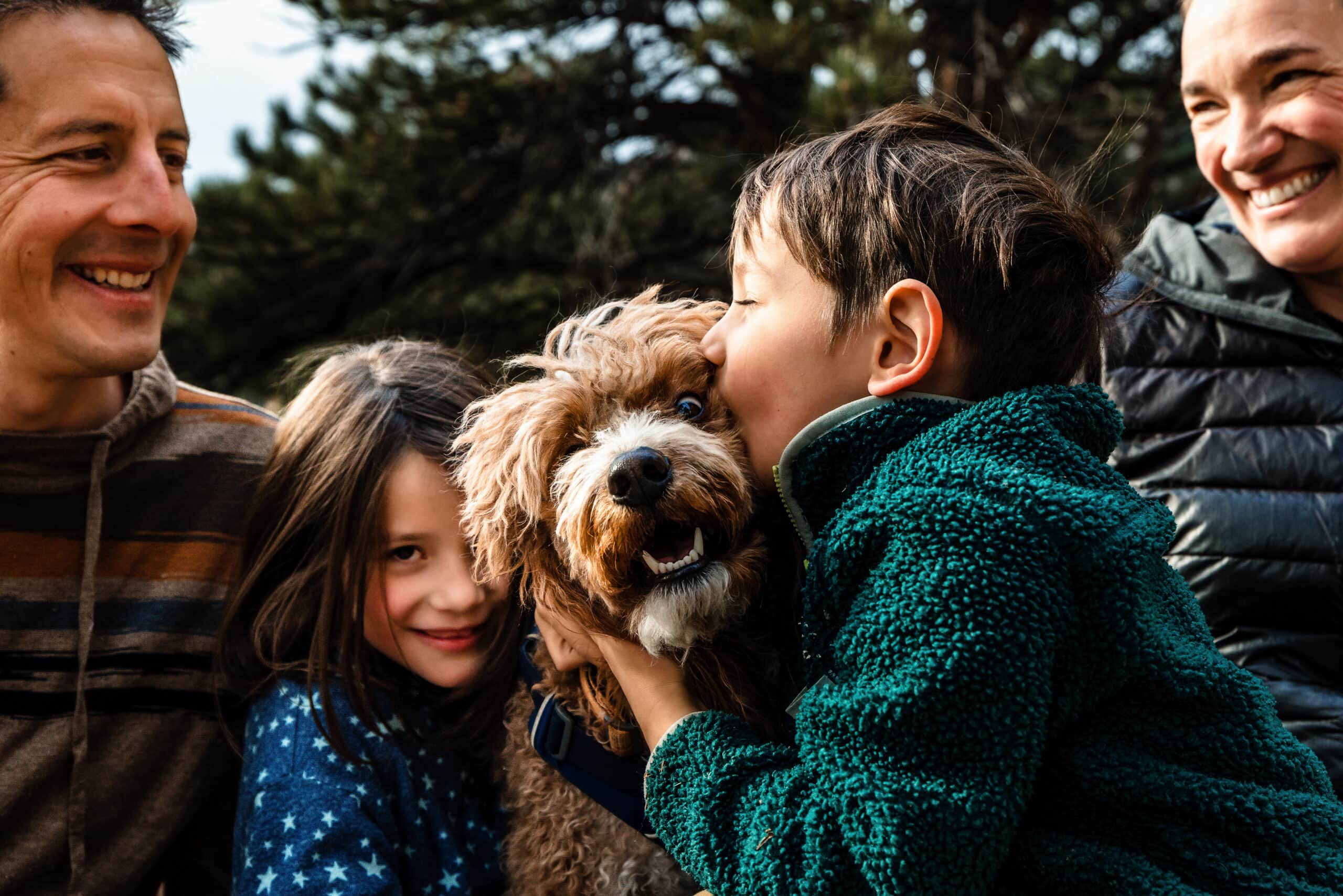 Smiling family cuddles curly dog outdoors in candid natural light portrait