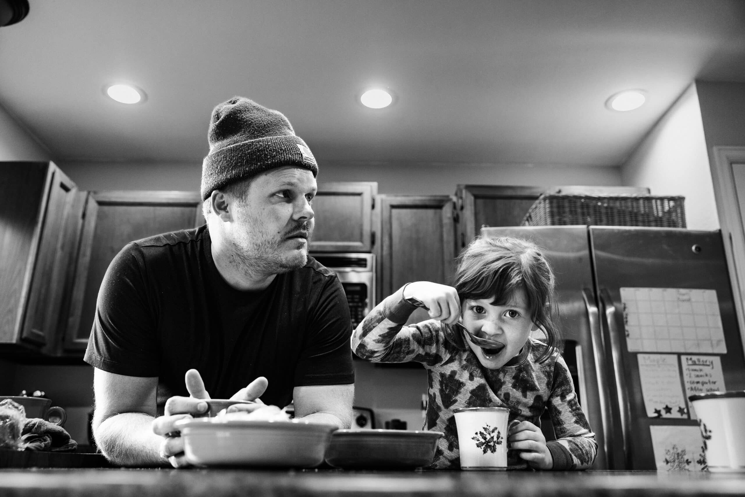 Black-and-white candid of parent and child eating breakfast in a home kitchen.