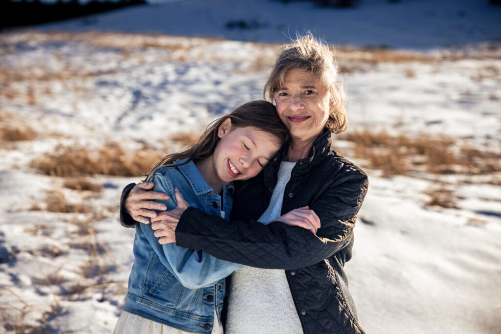 Grandmother and granddaughter hugging in a snowy field at sunset