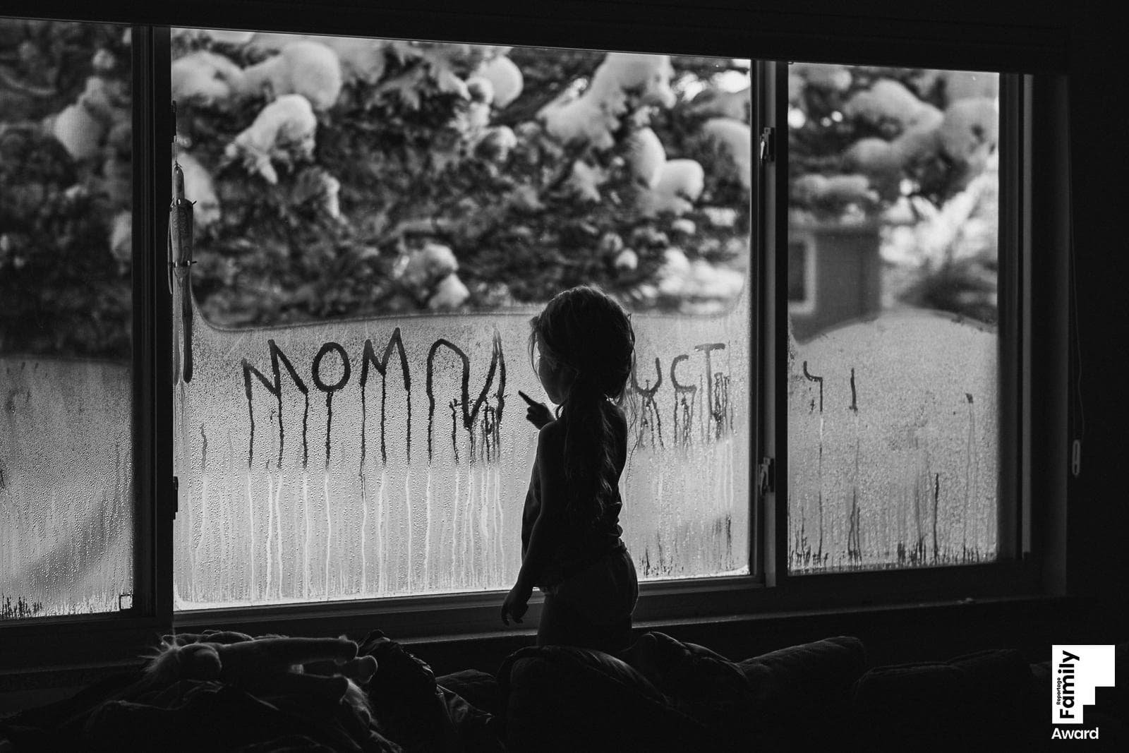 Silhouetted child writes Mom on foggy snowy window in black and white