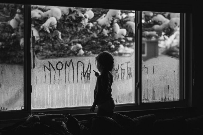Silhouetted child writes on foggy winter window in black-and-white family documentary photo
