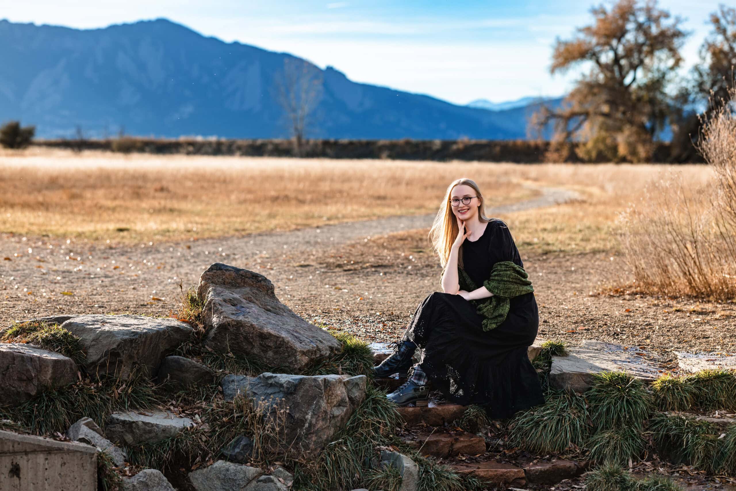 High school senior girl in a black dress with green sweater getting her senior pictures taken.