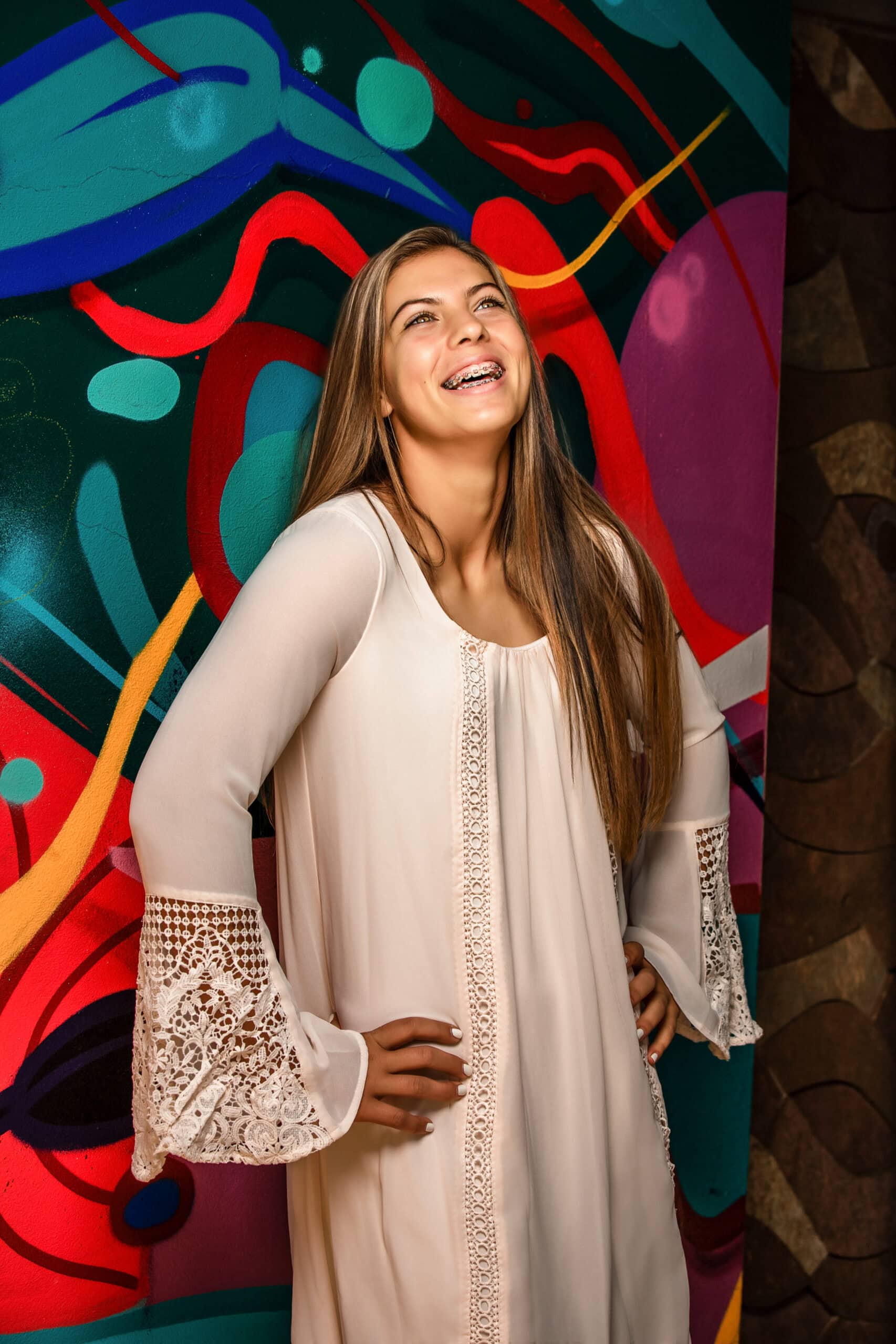 Colorado senior pictures with smiling graduate in cream lace dress by colorful Boulder mural
