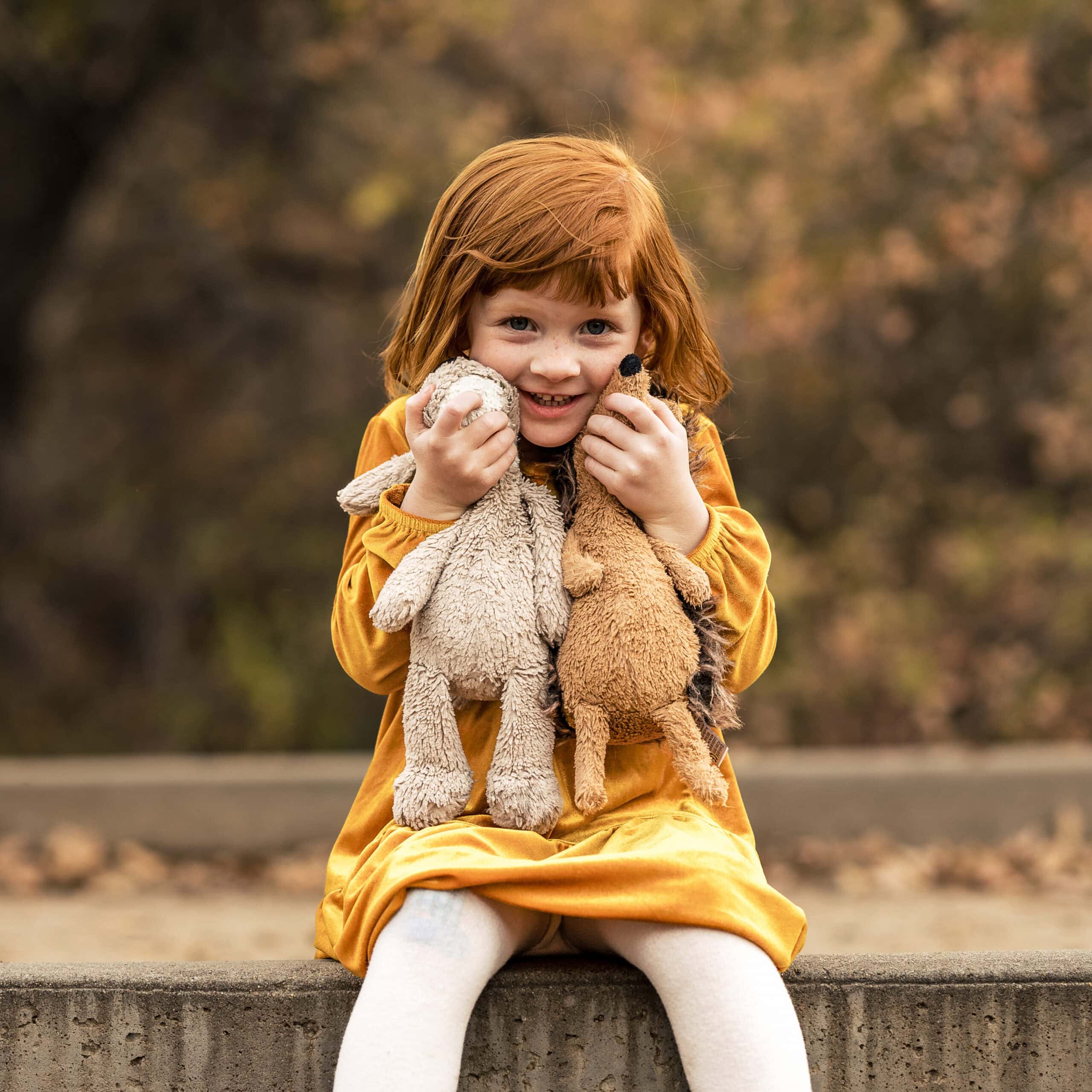 Smiling red-haired child cuddling stuffed rabbits outdoors in autumn
