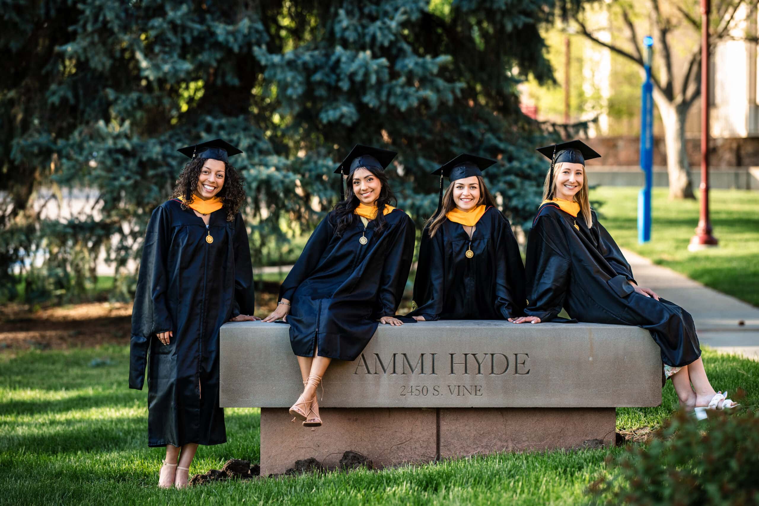 Colorado Senior Pictures of four friends in caps and gowns on a campus bench