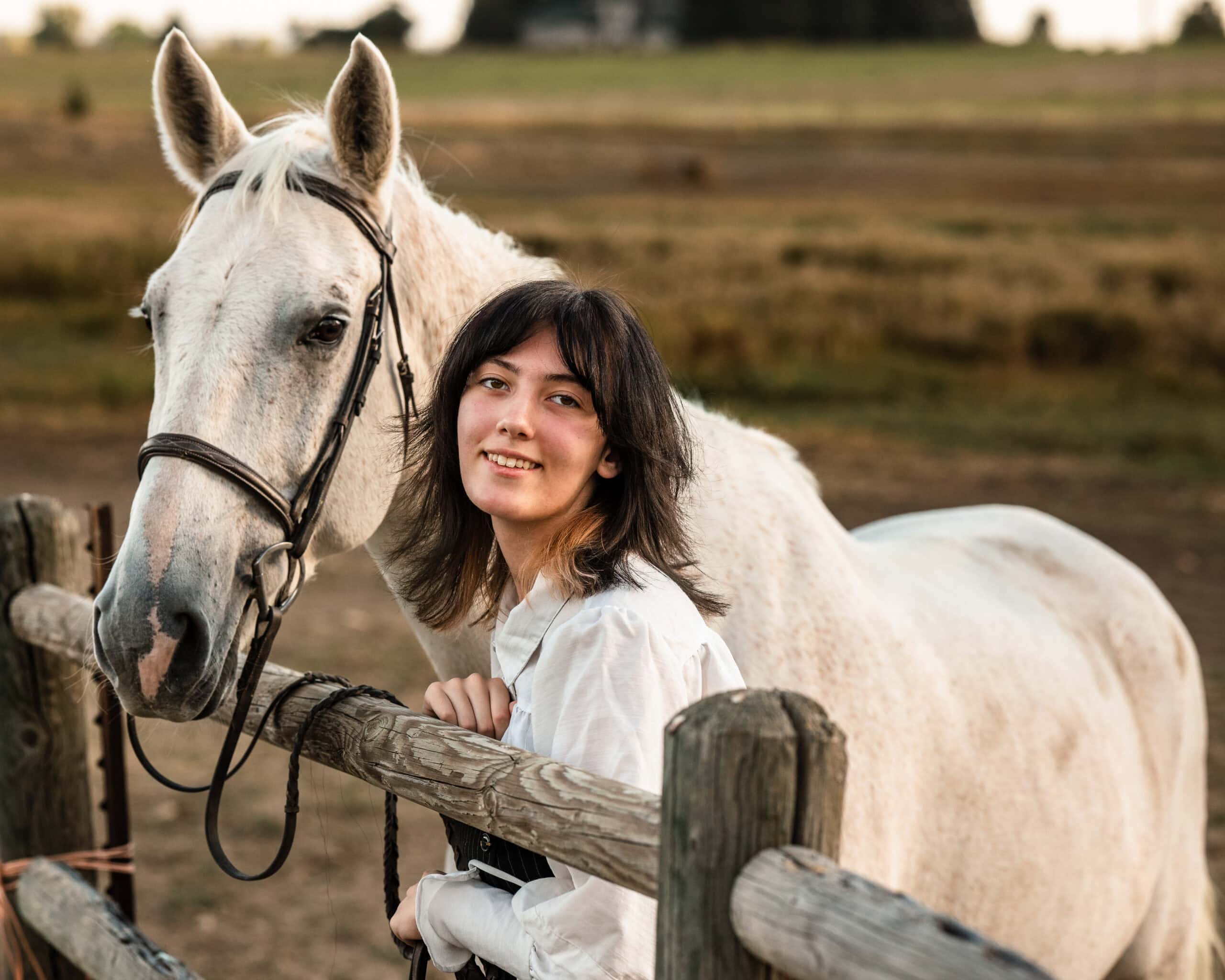 Colorado senior pictures portrait with smiling woman and gray horse by rustic pasture fence
