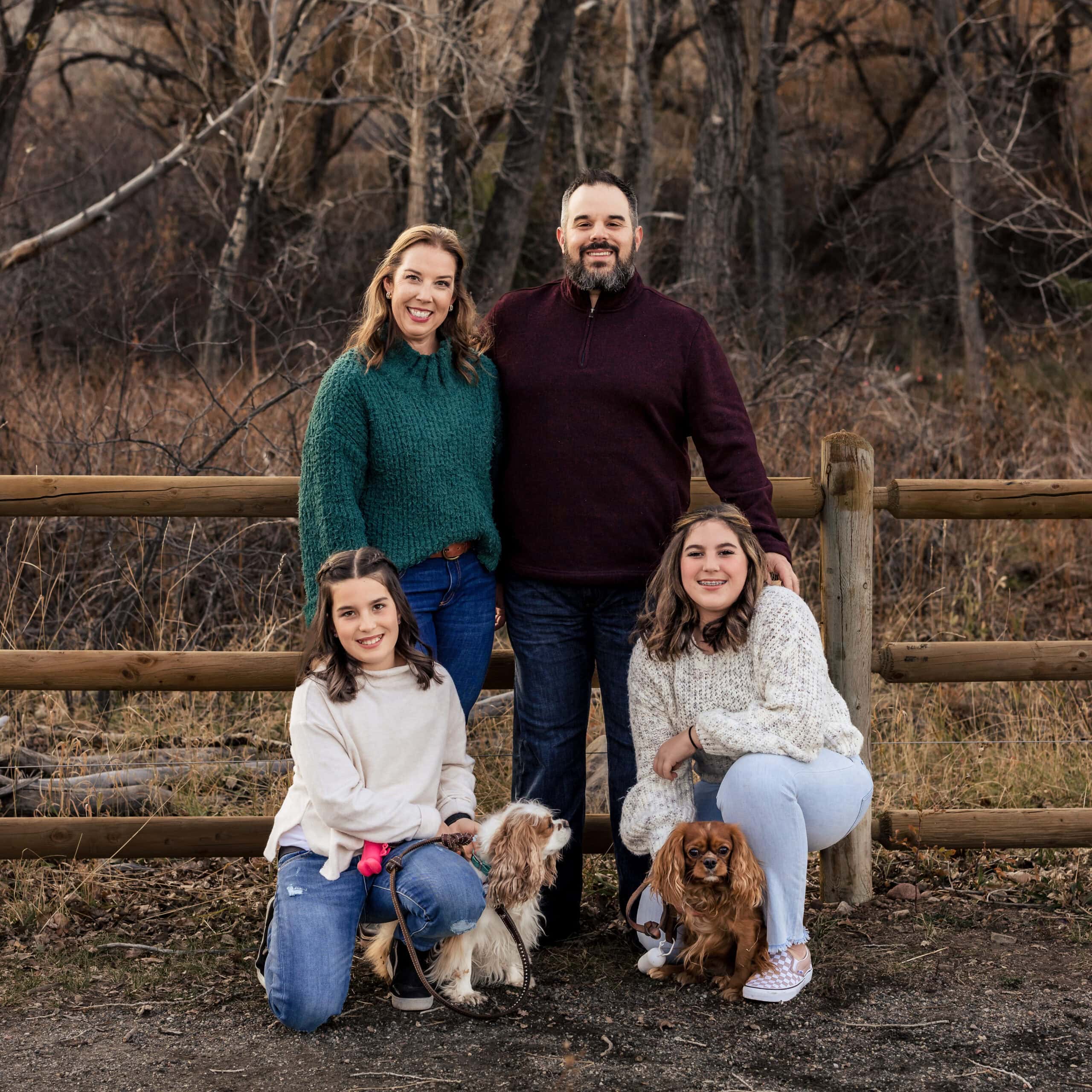 Outdoor family portrait with two dogs by a rustic wooden fence