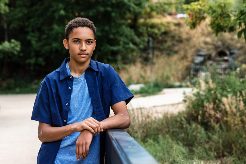 Outdoor Boulder Colorado senior portrait leaning on railing with soft green foliage