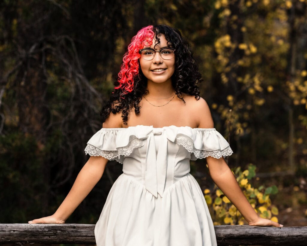 Senior photographer Boulder Colorado portrait of smiling teen in white dress by rustic railing