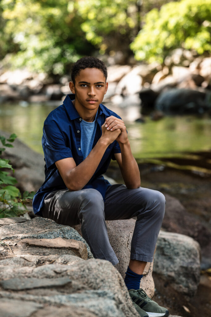 Senior portrait photographer Boulder Colorado captures teen seated on creek rocks in natural light.