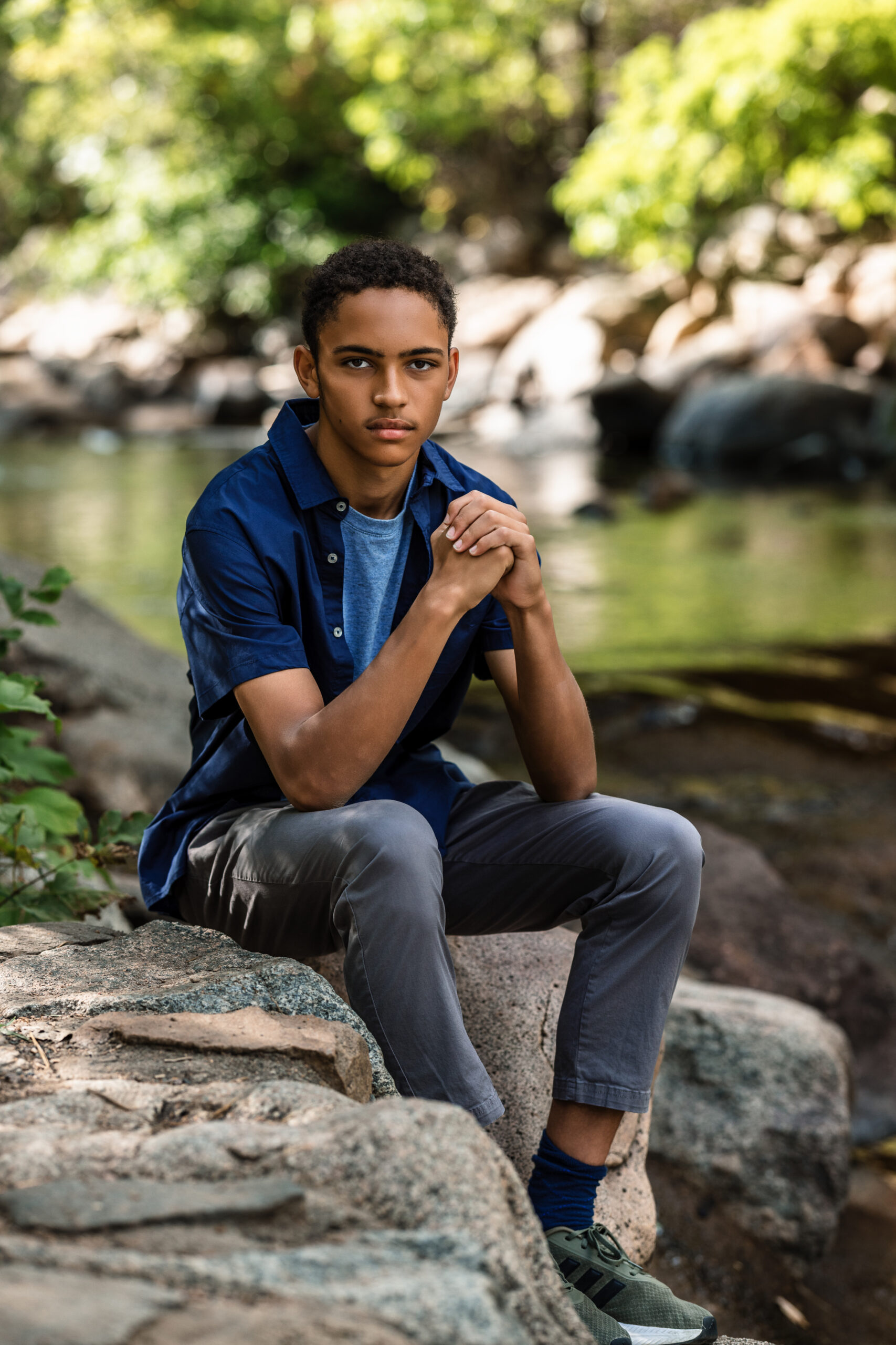 Senior portrait photographer Boulder Colorado captures teen seated on creek rocks in natural light.