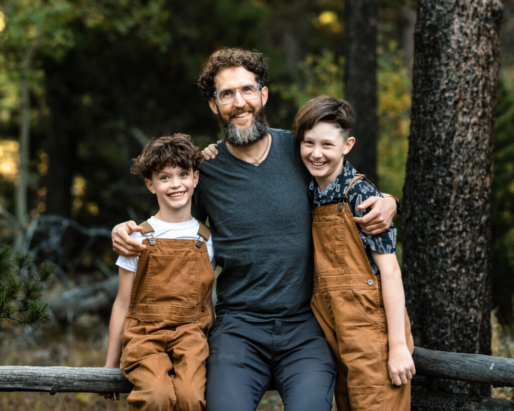 Fall Family Mini Sessions Colorado with dad and two boys smiling in wooded setting