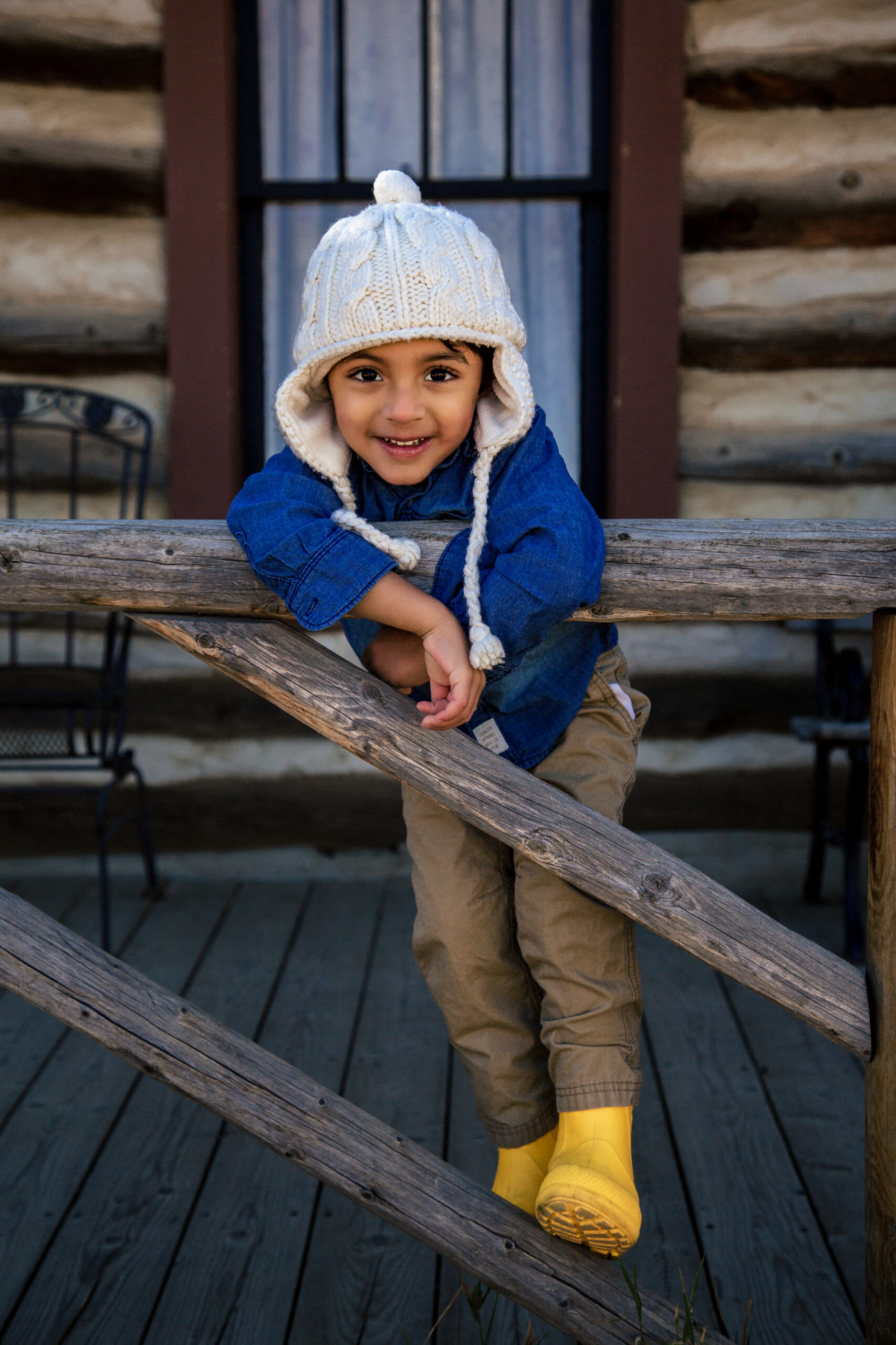 Smiling child in knit hat on rustic log cabin porch railing