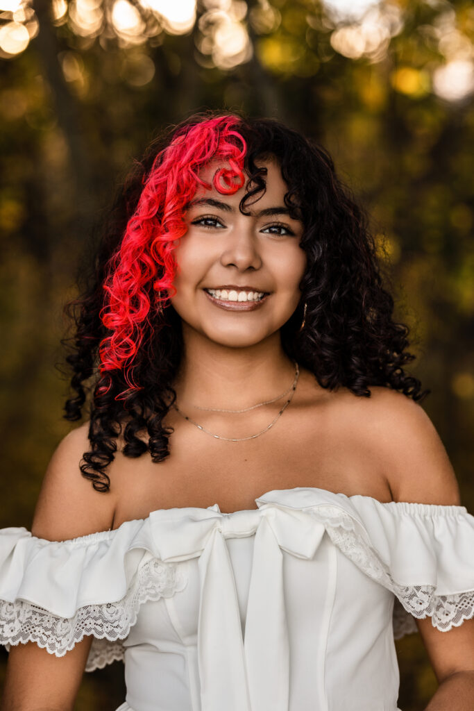 Senior photographer Boulder Colorado portrait of smiling student with red-streaked curls in golden hour