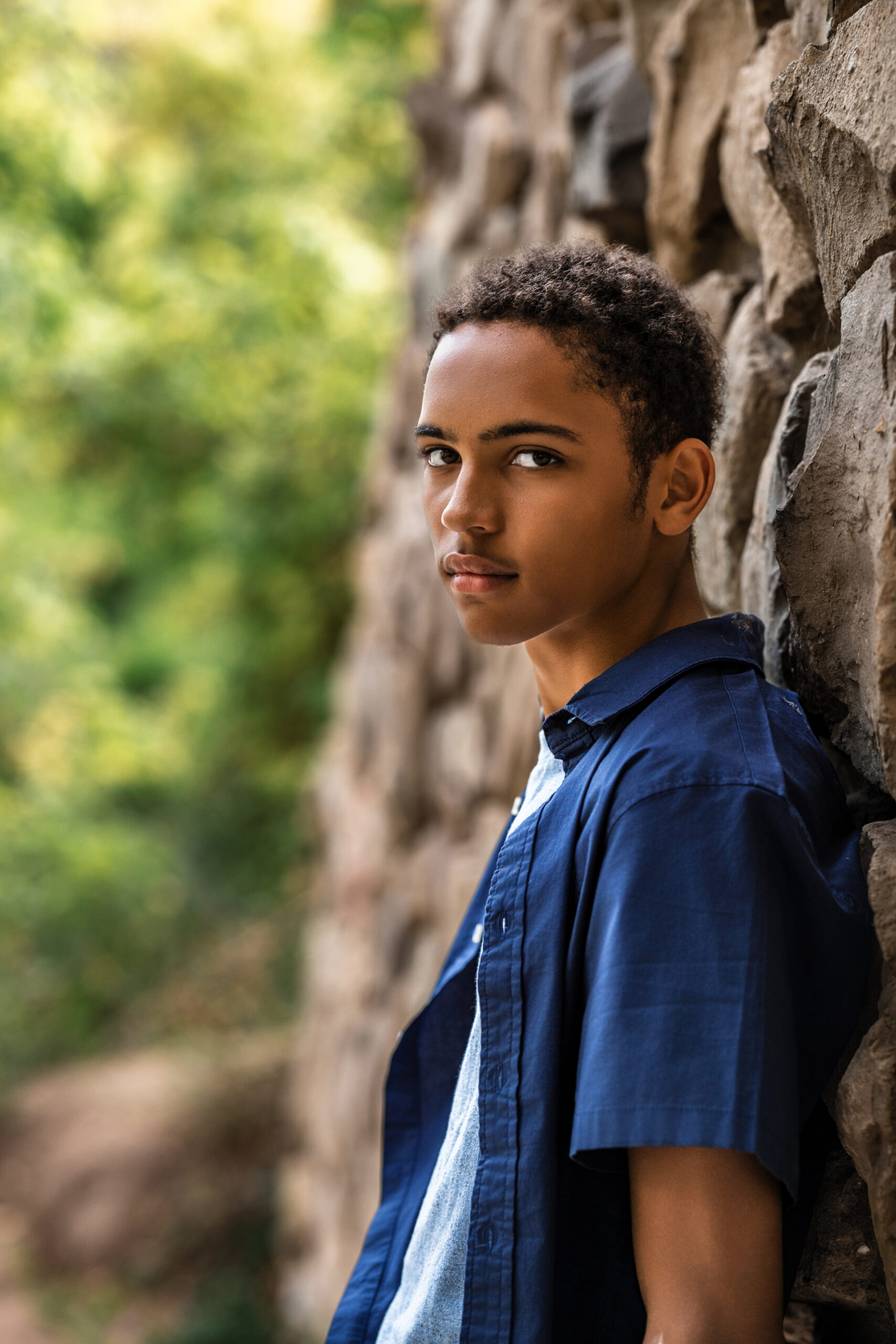 Senior portrait by Boulder Colorado photographer, student leaning against stone wall in natural light.
